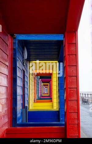 Una vista attraverso i portici di colorate capanne fronte spiaggia in legno sul lungomare della città costiera dello Yorkshire settentrionale di Saltburn-by-the-Sea in una giornata di inverni miti. Foto Stock