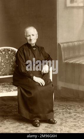 Una donna anziana che indossa un lungo vestito nero, i suoi capelli bianchi legati ordinatamente dietro in un panino, Foto Stock