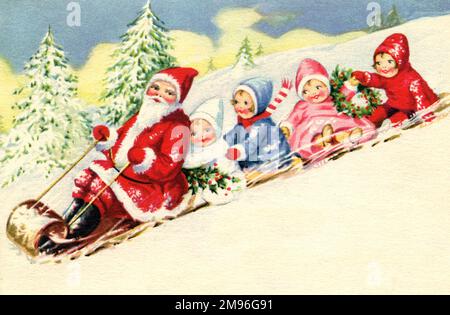 Babbo Natale scola giù una collina innevata accompagnata da quattro bambini felici che trasportano un ramo agrifoglio e una corona. Foto Stock