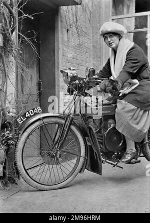 Una donna su una motocicletta Douglas a lato di una casa. Indossa un berretto grande e guanti enormi. Foto Stock