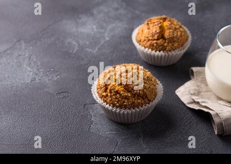 Deliziosi muffin fatti in casa alla zucca con crosta di zucchero piccante con latte su fondo testurizzato nero, spazio Foto Stock