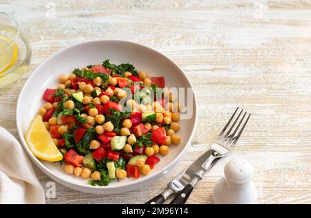 Insalata vegana sana con ceci, pomodori, cetrioli, peperoni e kale su sfondo di legno chiaro, spazio Foto Stock