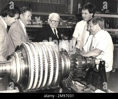 “Sir Frank Whittle (al centro) il pioniere dei motori a reazione, il cui primo motore funzionava con successo 50 anni fa, vide uno dei suoi discendenti diretti, il turbofan del V2500, a Rolls-Royce, Derby. Il modello V2500 è 18 volte più potente della prima unità Whittle (WU) ma utilizza meno di un terzo di carburante per libbra di spinta. Qui Sir Frank vede l'assemblaggio del rotore del compressore ad alta pressione. La prima WU è stata eseguita il 12 aprile 1937 presso la compagnia Power Jets di Whittle a Lutterworth, a soli 35 km da dove si trova oggi lo stabilimento di Rolls-Royce Derby”. 13 agosto 1987. Foto Stock