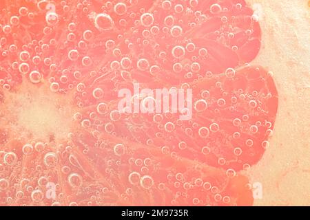 Fetta di pompelmo rosso che galleggia nella soda del club. Fetta di pompelmo fresco con bolle nella bevanda gassata. Fetta di pompelmo rosso naturale fresco di bubb Foto Stock