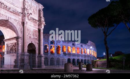 Una vista diversa del Colosseo romano di notte quando è illuminato dall'interno. L'arco di Costantino e giardino. Foto Stock