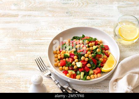 Insalata vegana sana con ceci, pomodori, cetrioli, peperoni e kale su sfondo di legno chiaro, spazio Foto Stock