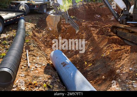 L'operatore che utilizza il trattore solleva i tubi delle acque reflue nel terreno si prepara a installare tubi di calcestruzzo interrati Foto Stock