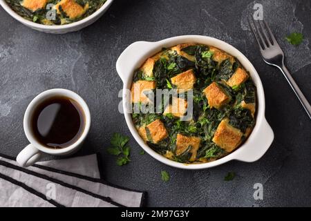 Frittata verde al forno con spinaci e crostini, in forma bianca su fondo testurizzato scuro, piatto Foto Stock