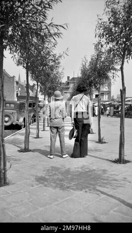 Due persone camminano lungo un marciapiede alberato. Foto Stock