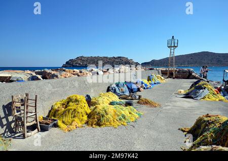 Plaka, Creta, Grecia - 10 ottobre 2022: Famiglia non identificata sulla talpa con reti da pesca e barche nel porto di Plaka con la fortezza di Spinalonga, Foto Stock