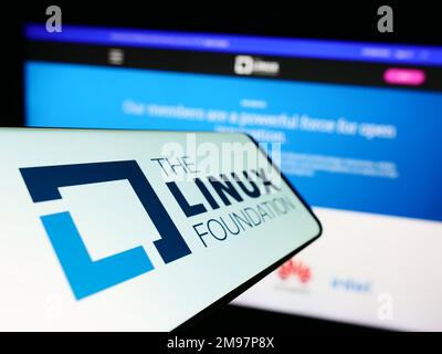 Telefono cellulare con il logo del consorzio di tecnologia Linux Foundation sullo schermo di fronte al sito web. Messa a fuoco al centro a sinistra del display del telefono. Foto Stock