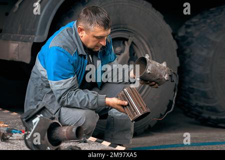 Riparazione meccanica del veicolo. Riparazione e diagnostica professionale di trattori e attrezzature cargo. Il meccanico in officina considera i pezzi di ricambio. Foto Stock