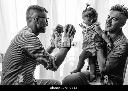 Coppia gay maschile con la bambina adottata a casa - due bei padri che giocano con la loro figlia - famiglia LGBTQ+ a casa - Diversity Concept e LGBT Foto Stock