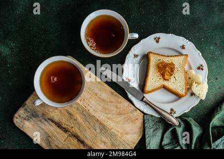 Vista dall'alto di due tazze di tè e una fetta di pane tostato con marmellata Foto Stock