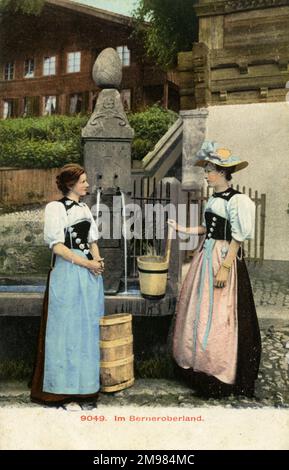 Berna, Svizzera - due donne nell'Oberland Bernese (Highlands Bernesi), che raccolgono l'acqua da una fontana pubblica indossando il costume tradizionale svizzero. Foto Stock