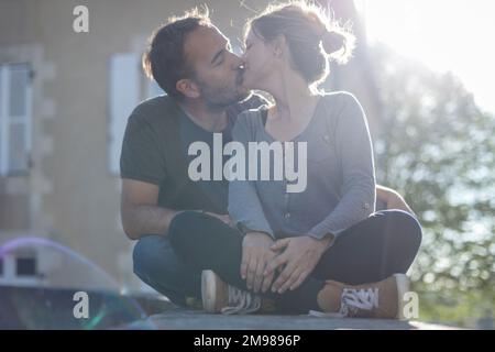 Coppia seduta a gambe incrociate su un muro di pietra in estate baciare, Francia Foto Stock