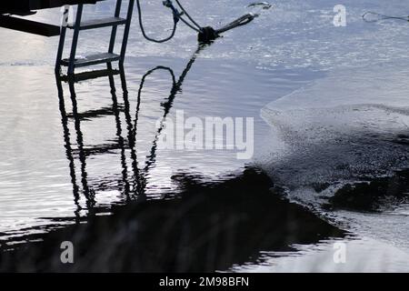 Riflessi da un piccolo molo in inverno. Acqua oceanica con sottile strato di ghiaccio, tonalità blu e grigio. Foto Stock