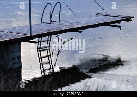 Piccolo molo d'inverno. Riflessi sull'acqua e sottile strato di ghiaccio. Scena tranquilla. Foto Stock