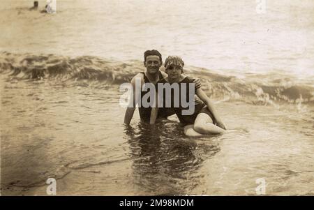 Giovane coppia seduta in surf - classico inglese mare candido fotografia - agosto, 1921. A meno che non sia un difetto sulla lastra fotografica (possibile) la giovane donna sembra avere un occhio nero - forse ha sottovalutato la posizione della lampada sospesa nella sala colazione della Mrs Miggins' Guesthouse a colazione quella mattina...! Foto Stock