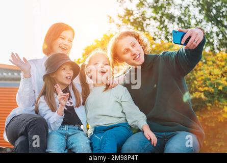 Ritratti di tre sorelle sorridenti e di un fratello adolescente che scattano un selfie utilizzando una moderna fotocamera per smartphone. Infaticabile felice giovane teenhood, infanzia Foto Stock