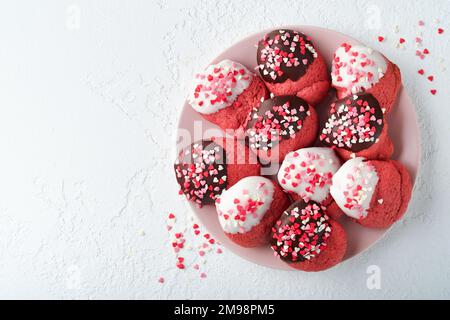 Biscotti di San Valentino. Biscotti frollini con cioccolato bianco e scuro glassato e cuore cosparsi in piatto rosa su fondo bianco. Giornata delle madri. WOM Foto Stock