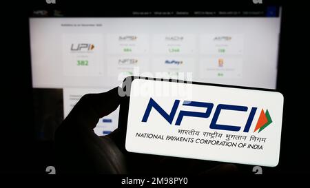 Persona che tiene il cellulare con il logo della National Payments Corporation of India (NPCI) sullo schermo di fronte al sito web. Messa a fuoco sul display del telefono. Foto Stock