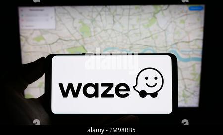 Persona che tiene il cellulare con il logo della società di navigazione israeliana Waze Mobile Ltd. Sullo schermo di fronte al sito web aziendale. Messa a fuoco sul display del telefono. Foto Stock