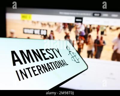 Telefono cellulare con il logo dell'organizzazione per i diritti umani Amnesty International sullo schermo di fronte al sito web. Messa a fuoco al centro a sinistra del display del telefono. Foto Stock