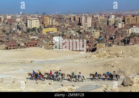 CAIRO, EGITTO - 28 GENNAIO 2019: I turisti cavalcano i cavalli di fronte alle piramidi con lo sfondo della città di Giza, Egitto Foto Stock