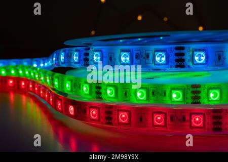 Set di strisce LED colorate a inseguimento con luci verdi e blu al neon luminose posizionate sul tavolo in una stanza buia Foto Stock