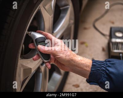 Controllo meccanico degli pneumatici per auto per verificarne il corretto gonfiaggio. Uomo che utilizza un manometro digitale per controllare la pressione dell'aria degli pneumatici della vettura. Foto Stock