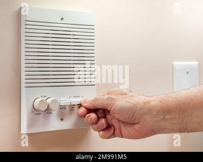 Rispondere al campanello e parlare sul sistema di comunicazione intercom domestico. Primo piano della mano maschile che spinge il sistema di sicurezza a casa pulsante di conversazione. Foto Stock