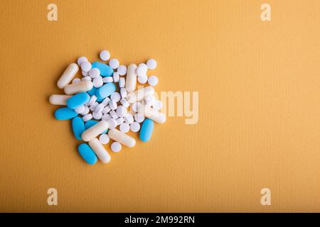 Un'inquadratura ad angolo alto di medicinali ovali blu e bianchi su sfondo giallo. Foto Stock