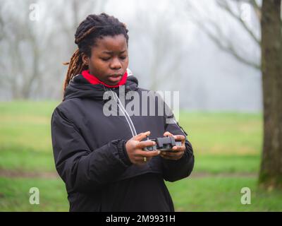 Allegro giovane teencaer afroamericano vestito di abbigliamento sportivo che vola un drone in un parco. Foto Stock