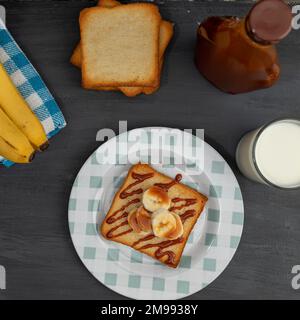 vista dall'alto di un pane tostato con banana e cajeta e un bicchiere di latte. Foto Stock