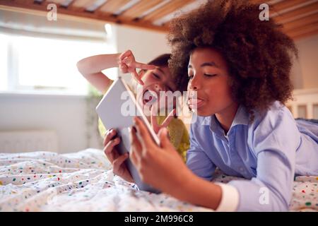 Ragazza e ragazzo in camera da letto sdraiati sul letto utilizzando il tablet digitale e tirando le facce divertente insieme Foto Stock