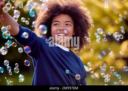 Sorridere Boy Outdoors divertirsi giocando con le bolle in giardino Foto Stock
