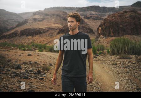 Un giovane barbuto cammina su una selvaggia strada di campagna occidentale Foto Stock