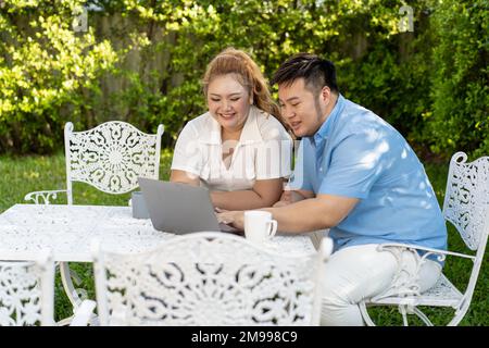 Giovane coppia asiatica chubby utilizzando un computer portatile nel parco verde all'aperto insieme. Felice uomo sorridente e donna che lavorano a distanza e avviare il proprio business insieme Foto Stock