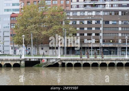 Si affaccia sul fiume Nervíon a Bilbao, Paesi Baschi, con edifici dietro e un'arte di strada piastrellata Invader sul bordo che conduce alla riva Foto Stock