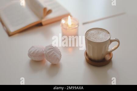 tazza di caffè, fiore, candela e un libro su un tavolo bianco sfondo vista dall'alto Foto Stock