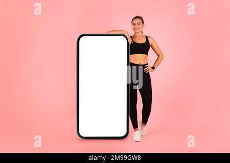 App allenamento Bella giovane donna in Sportswear Pendente a Big Blank smartphone Foto Stock
