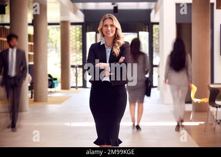 Ritratto del CEO maturo di Businesswoman in piedi nella lobby di occupato edificio moderno di uffici Foto Stock