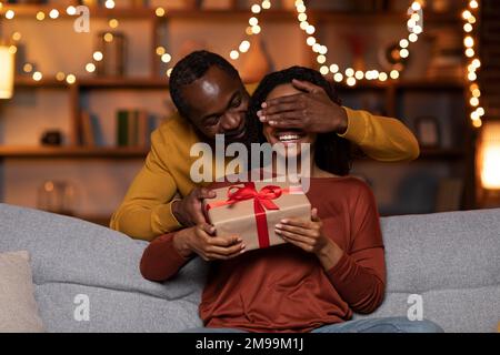 L'uomo nero amorevole saluta la moglie con il compleanno a casa, il marito  che dà la sua scatola regalo e sorridente, seduto insieme sul divano Foto  stock - Alamy