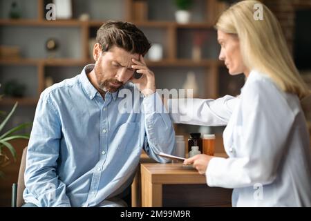 Diagnosi errata. La signora del medico che conforta il paziente maschio depresso durante l'appuntamento in clinica Foto Stock