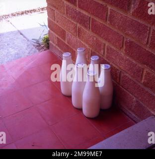 Sei bottiglie di latte con tappo in argento sul gradino di accesso. Foto Stock