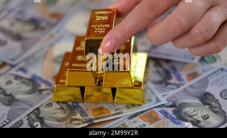 Mano umana che organizza pila di barre d'oro su banconote in dollari Foto Stock