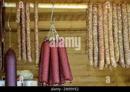 Salsiccia e altre prelibatezze affumicate a base di carne di diversi colori e dimensioni sono impilate sul banco. Commercio equo e solidale di specialità di carne fatte in casa. Primo piano. Sele Foto Stock