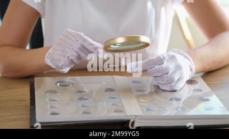 Numismatico in guanti esamina la collezione di monete attraverso la lente d'ingrandimento. Foto Stock