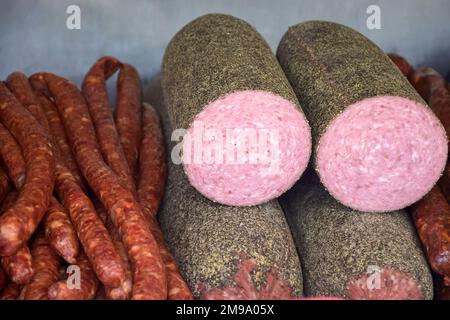 Salsiccia e altre prelibatezze affumicate a base di carne di diversi colori e dimensioni sono impilate sul banco. Commercio equo e solidale di specialità di carne fatte in casa. Primo piano. Sele Foto Stock